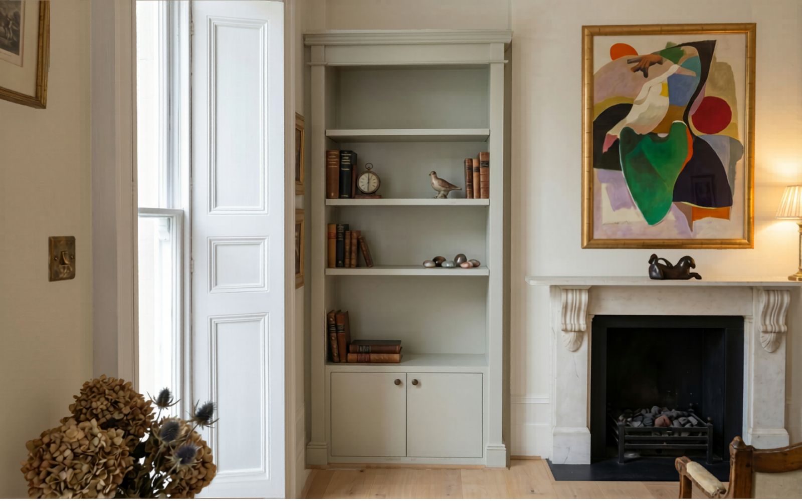 Bespoke fitted alcove bookcase with open shelves, lower cabinet and soft painted finish beside a traditional fireplace.