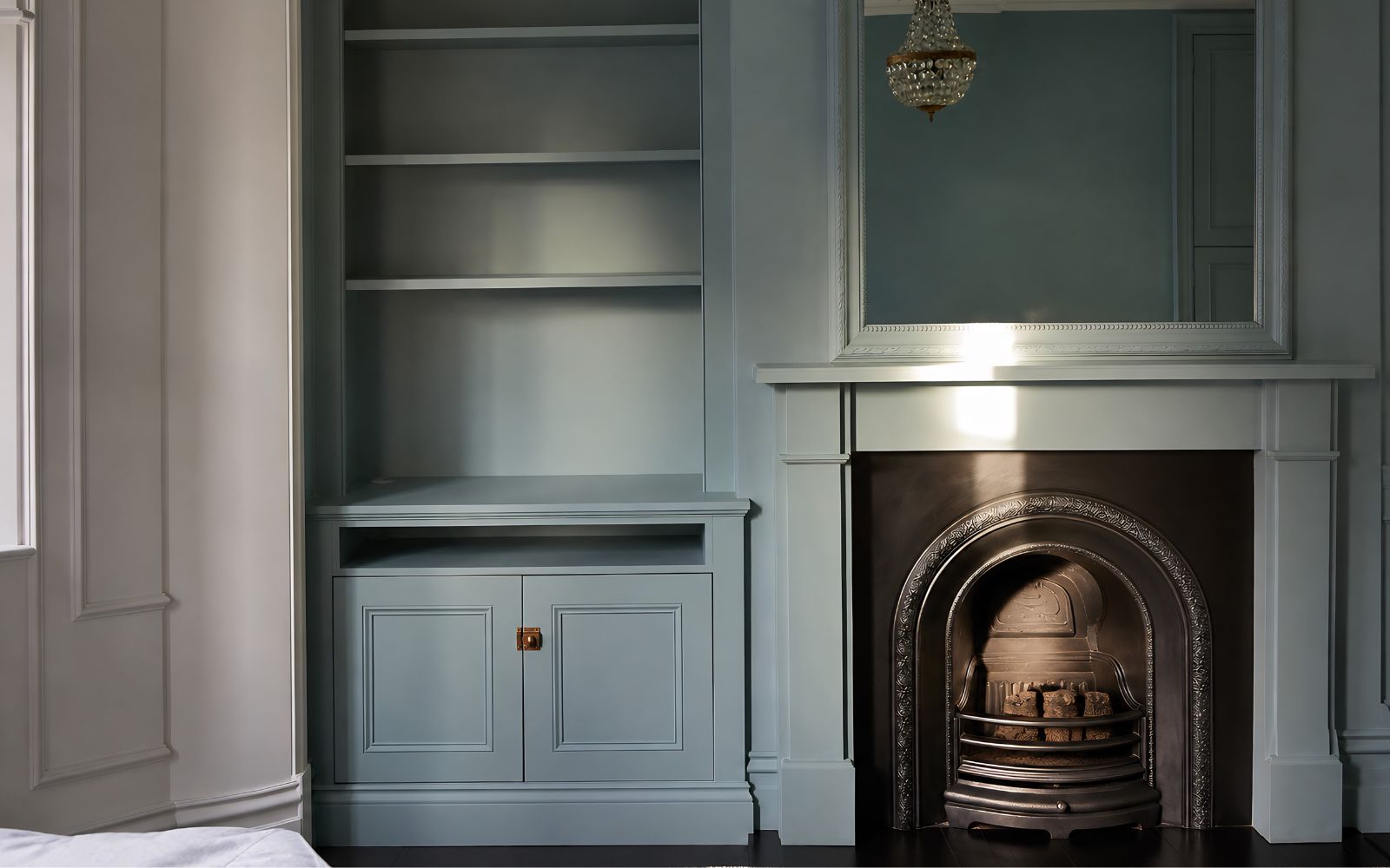 Bespoke blue-grey alcove cabinet with open shelves, lower panelled doors and traditional fireplace beside it.