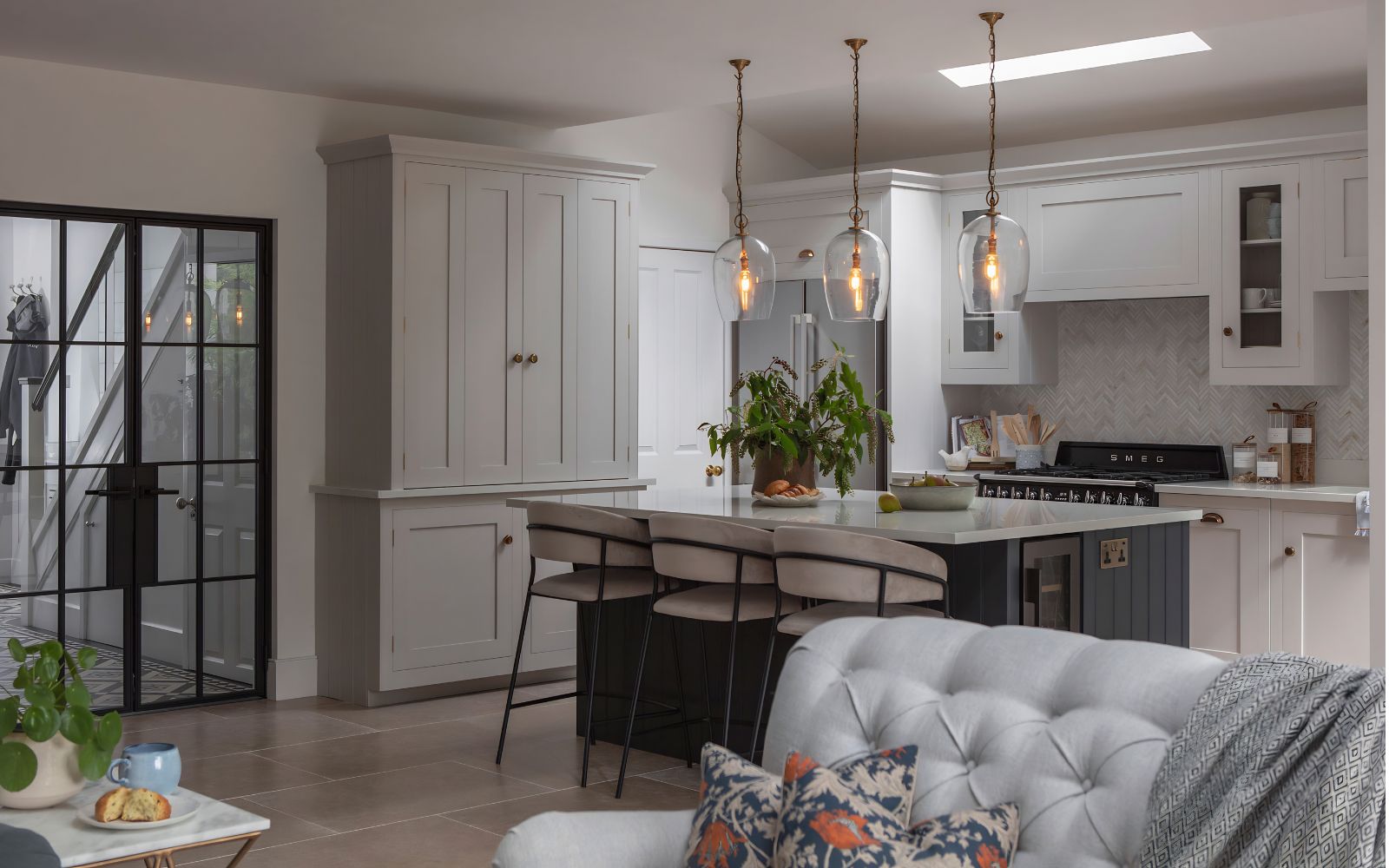Bespoke painted shaker kitchen with dark island, stone worktops, tall pantry cabinets, range cooker and pendant lights.